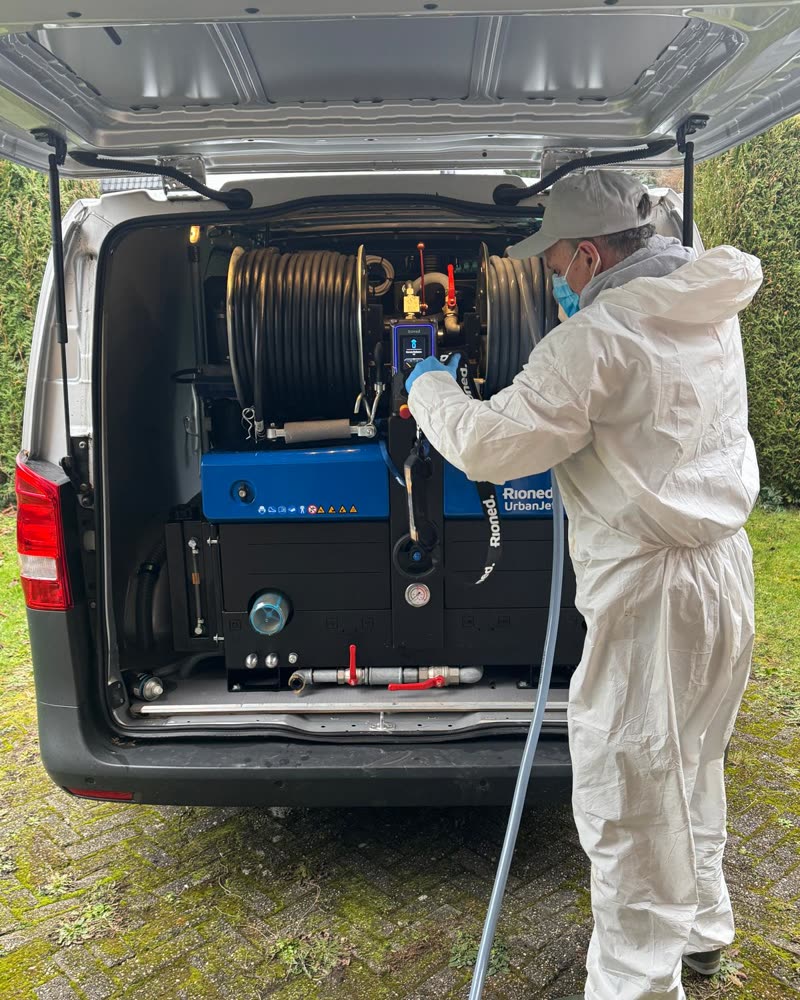 Technicien en tenue de protection devant la machine haute pression, à l'arrière de la camionnette.
