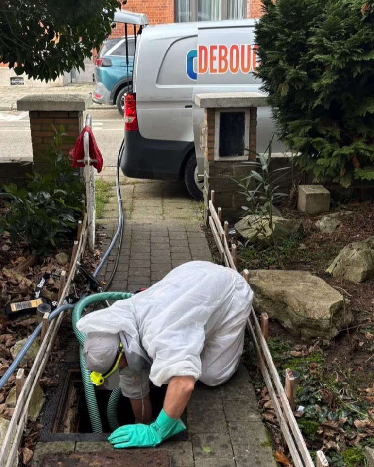 Technicien penché dans une chambre de visite devant une maison, la camionnette est garée dans la rue.