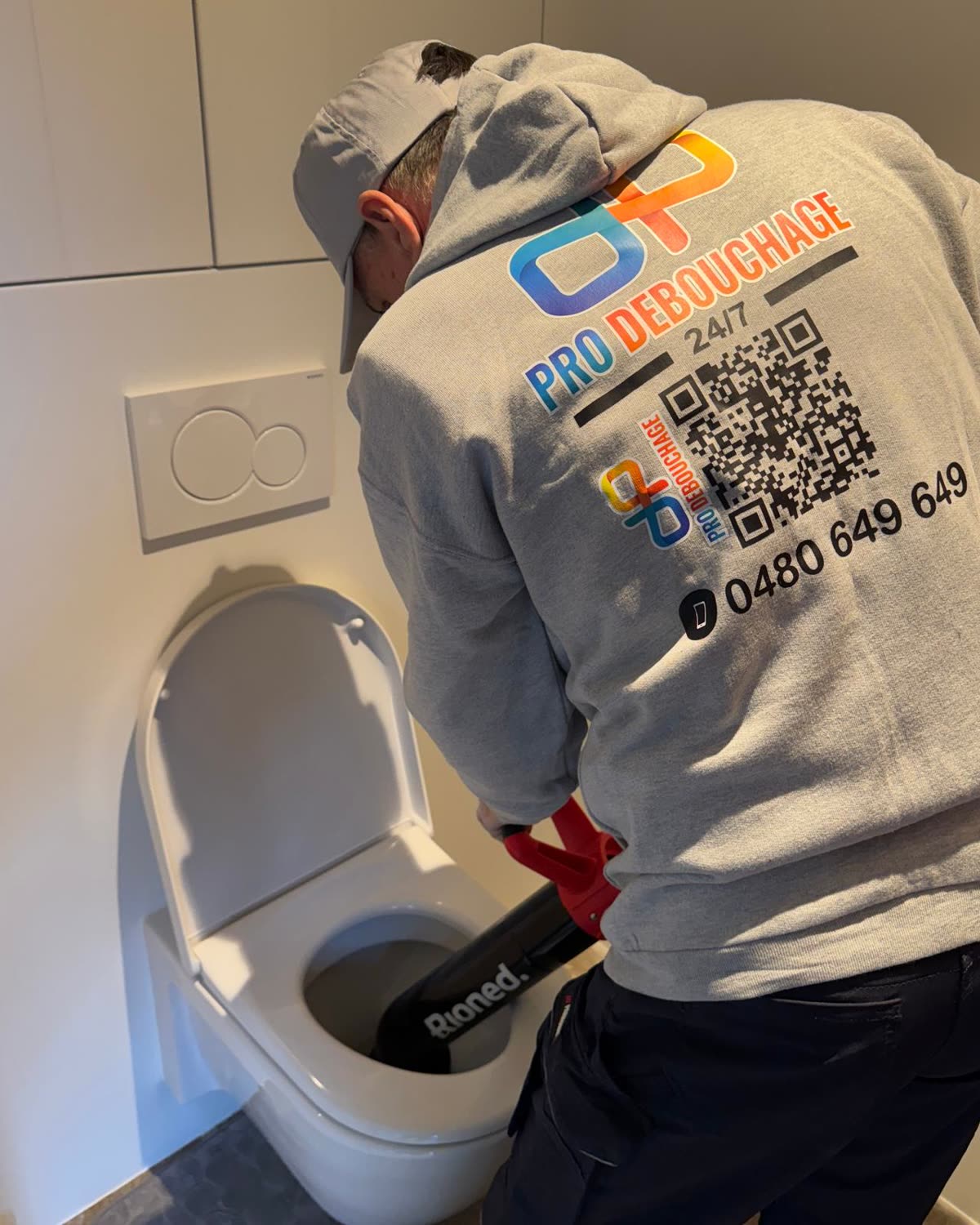 Technicien qui débouche un WC avec un furet, veste Pro Débouchage.